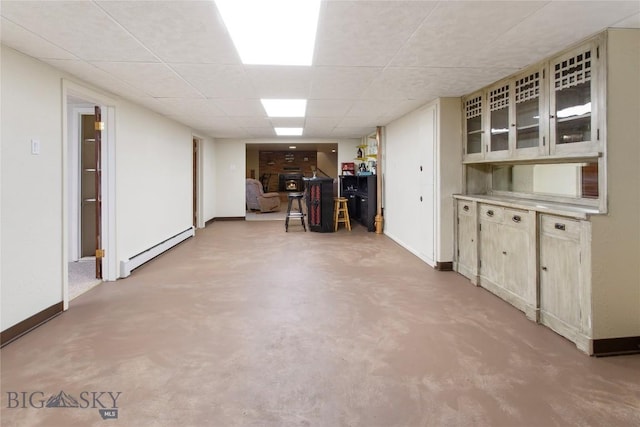 finished below grade area with a paneled ceiling, a baseboard radiator, and baseboards