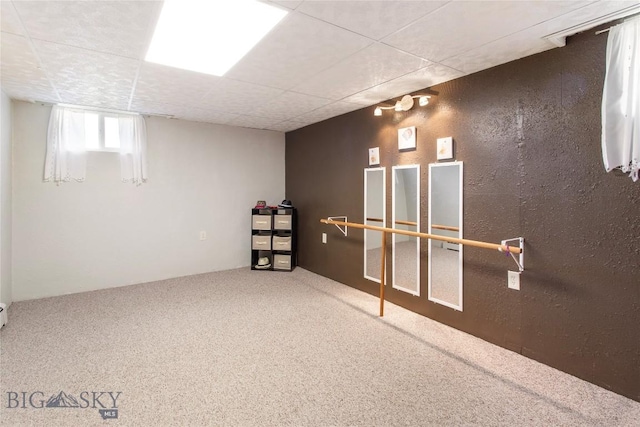 basement with a paneled ceiling, carpet flooring, and a textured wall