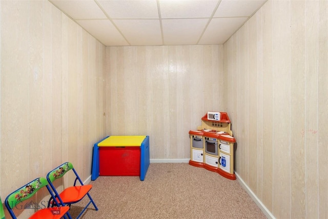 recreation room featuring a drop ceiling, wood walls, and carpet flooring