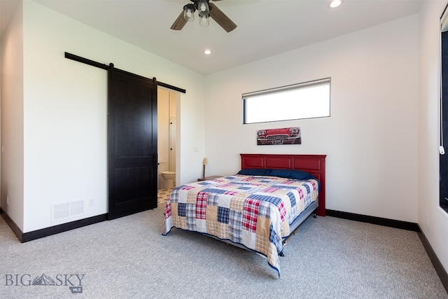 carpeted bedroom with ensuite bathroom, a barn door, and ceiling fan