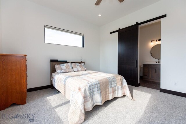 bedroom featuring light carpet, connected bathroom, a barn door, and ceiling fan