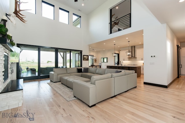 living room with a fireplace, a towering ceiling, sink, and light wood-type flooring