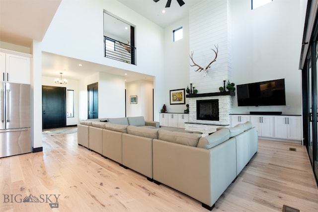 living room with light hardwood / wood-style floors, a fireplace, ceiling fan with notable chandelier, and a high ceiling