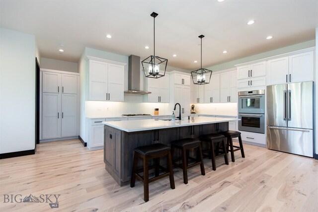 kitchen with white cabinets, stainless steel appliances, light hardwood / wood-style flooring, and wall chimney exhaust hood