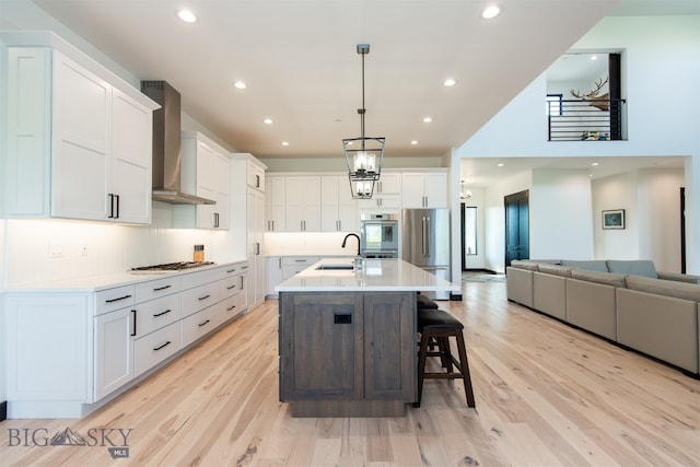 kitchen with wall chimney range hood, sink, white cabinets, and light hardwood / wood-style floors