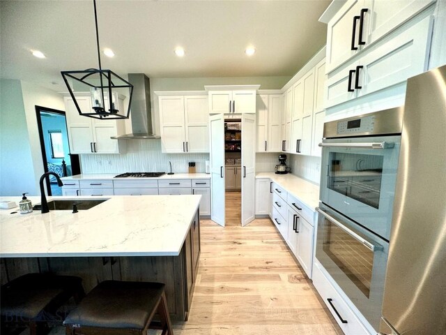 kitchen with white cabinetry, tasteful backsplash, wall chimney range hood, appliances with stainless steel finishes, and light hardwood / wood-style flooring