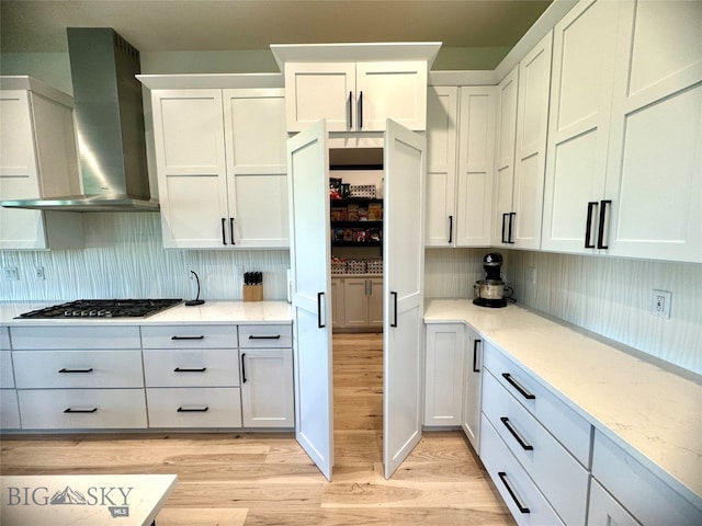 kitchen with light hardwood / wood-style floors, tasteful backsplash, white cabinets, and wall chimney exhaust hood