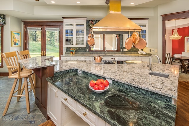 kitchen with a kitchen breakfast bar, light stone countertops, island range hood, black cooktop, and white cabinets