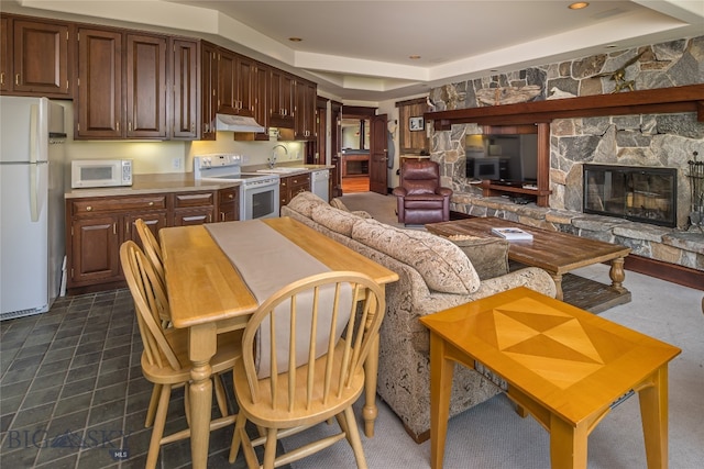 kitchen featuring a stone fireplace, white appliances, sink, and a raised ceiling