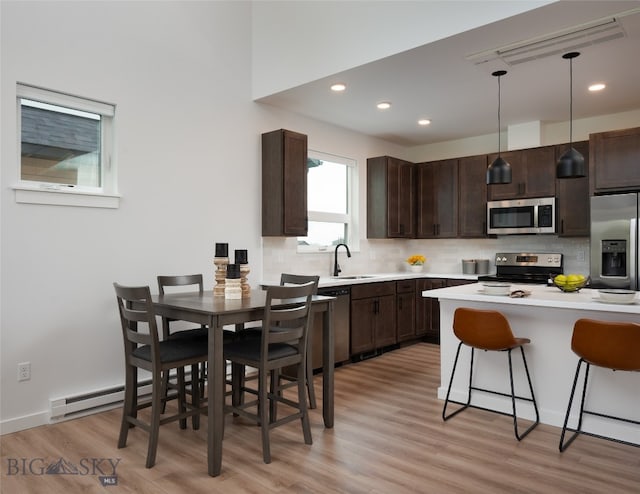 kitchen featuring appliances with stainless steel finishes, light hardwood / wood-style flooring, a breakfast bar, pendant lighting, and dark brown cabinetry