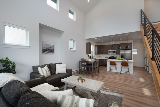 living room featuring wood-type flooring, sink, a wealth of natural light, and a towering ceiling