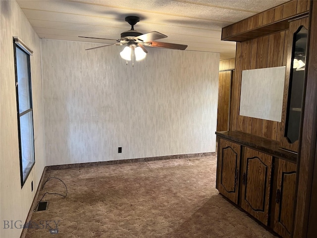 carpeted spare room with wood walls and ceiling fan