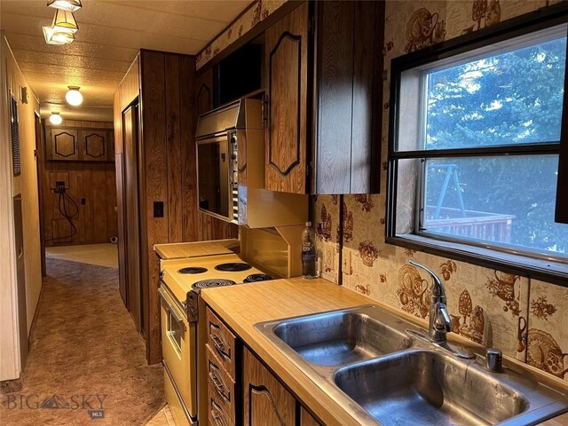 kitchen featuring sink, wooden walls, and white electric range oven