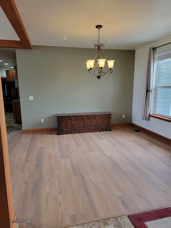 spare room featuring an inviting chandelier and light hardwood / wood-style floors