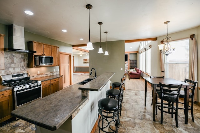 kitchen featuring sink, a kitchen bar, wall chimney exhaust hood, stainless steel appliances, and decorative light fixtures