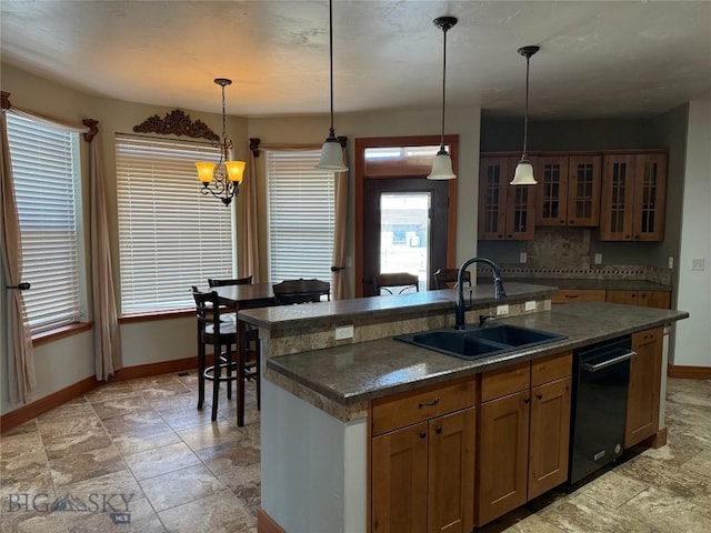 kitchen with a kitchen island with sink, a sink, baseboards, stone finish floor, and hanging light fixtures