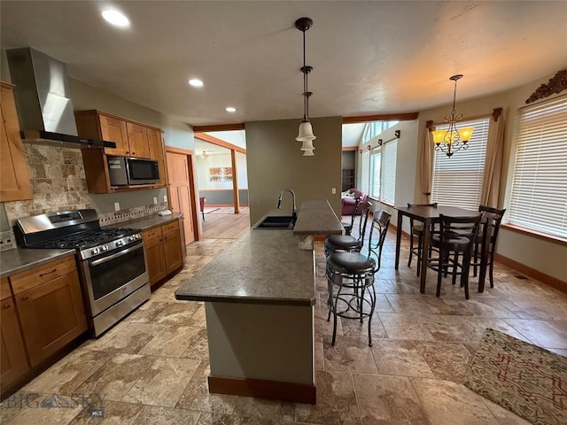 kitchen with wall chimney range hood, a sink, stone tile flooring, baseboards, and appliances with stainless steel finishes