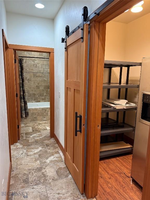 corridor with baseboards, stone finish floor, and a barn door