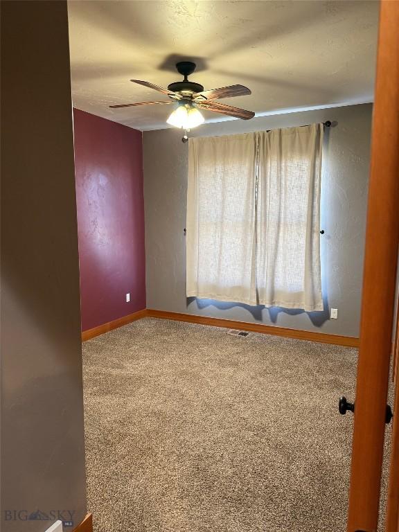 carpeted spare room featuring a ceiling fan and baseboards