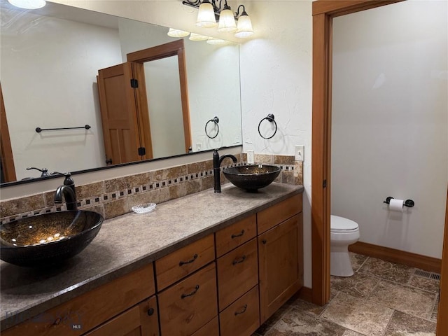 full bathroom with toilet, a notable chandelier, stone finish floor, and a sink