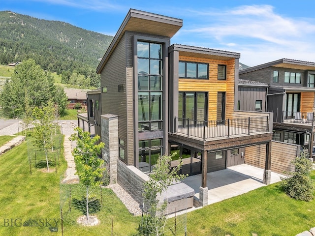 rear view of property featuring a mountain view, a balcony, and a lawn