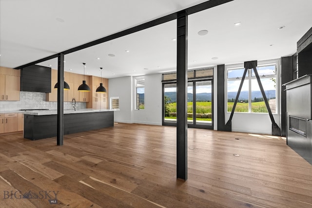 kitchen featuring backsplash, a kitchen island with sink, hardwood / wood-style floors, light brown cabinetry, and pendant lighting