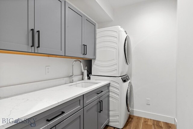 laundry area featuring sink, stacked washing maching and dryer, cabinets, and light hardwood / wood-style floors