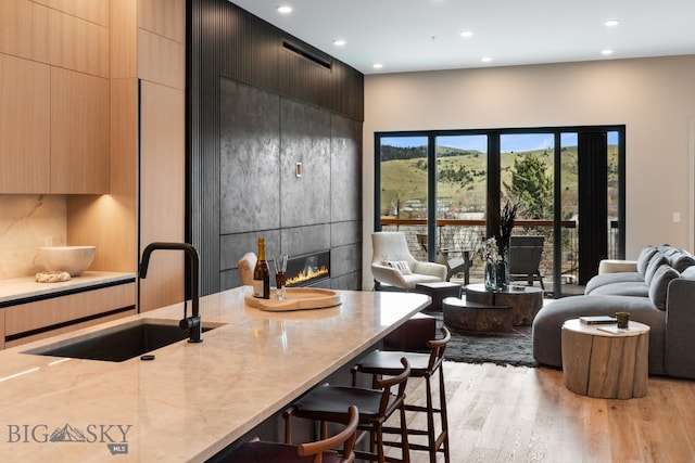 kitchen with a tile fireplace, a breakfast bar area, sink, light hardwood / wood-style flooring, and decorative backsplash