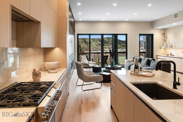 kitchen with light hardwood / wood-style floors, high end stove, light brown cabinets, and sink