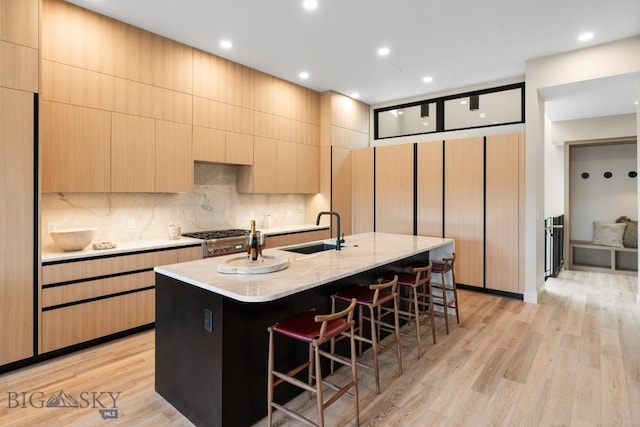 kitchen featuring light wood-style flooring, a breakfast bar, a sink, tasteful backsplash, and an island with sink