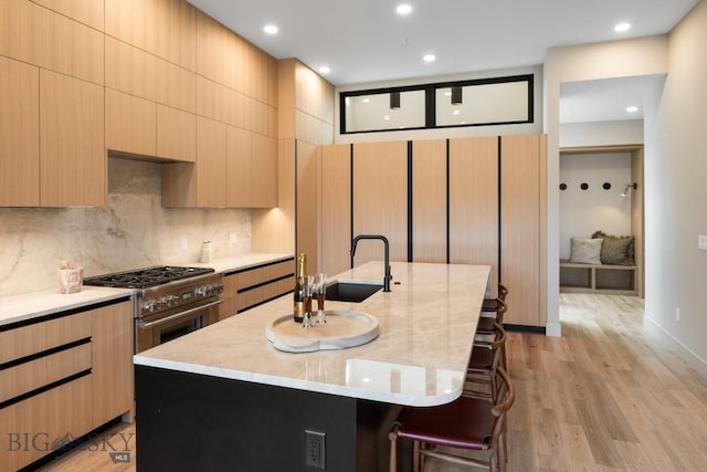 kitchen featuring light brown cabinets, a breakfast bar, a sink, backsplash, and stainless steel range