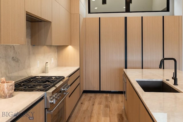 kitchen with light wood finished floors, tasteful backsplash, high end stainless steel range oven, a sink, and light stone countertops