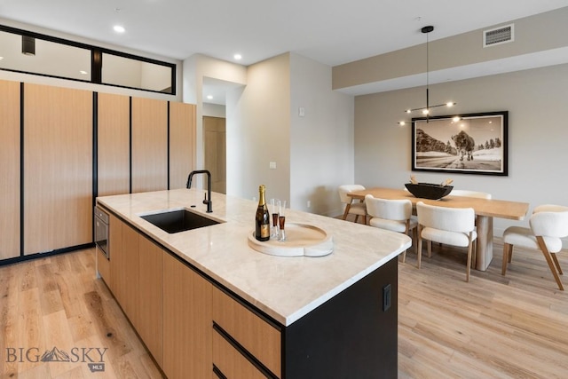 kitchen featuring a sink, visible vents, hanging light fixtures, light wood finished floors, and an island with sink