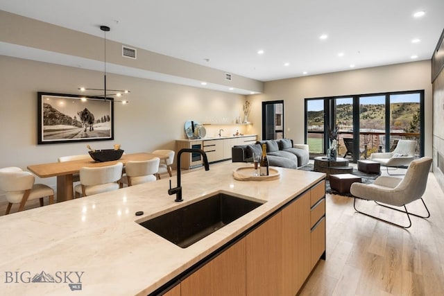 kitchen featuring light stone counters, light wood finished floors, visible vents, hanging light fixtures, and a sink