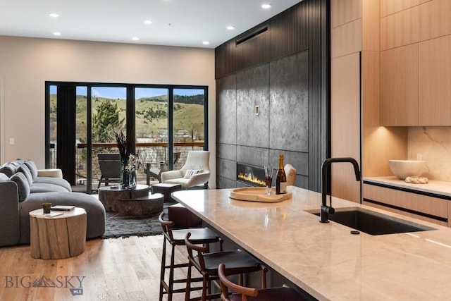 kitchen with a breakfast bar area, a tile fireplace, light wood-style flooring, a sink, and modern cabinets