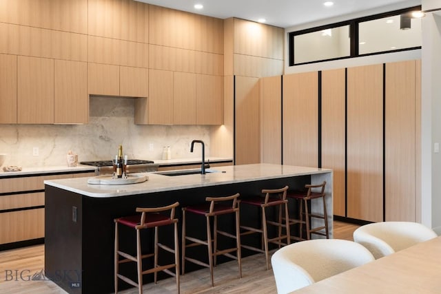 kitchen featuring a breakfast bar, tasteful backsplash, light wood-style flooring, a sink, and an island with sink