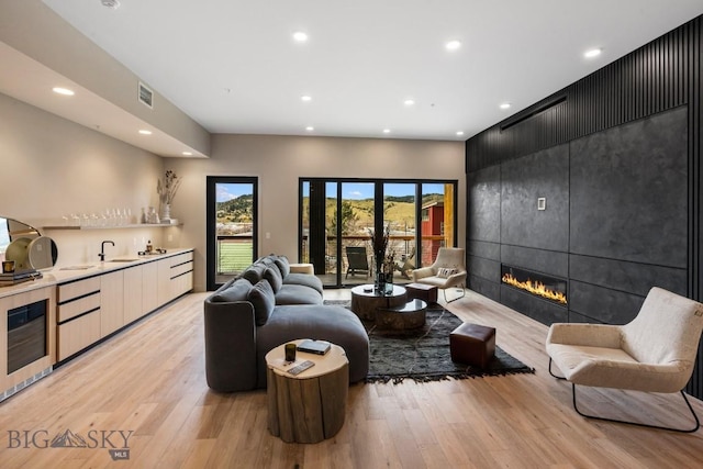 living area with recessed lighting, visible vents, light wood-style flooring, a tiled fireplace, and wet bar