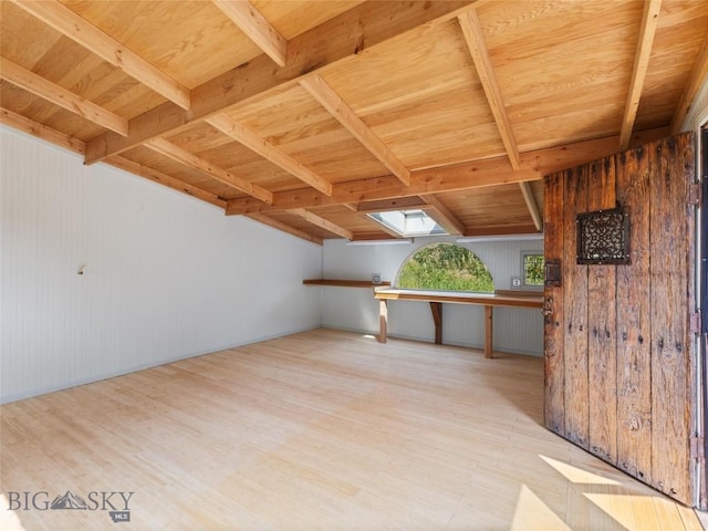 additional living space featuring wooden walls, a skylight, wooden ceiling, beam ceiling, and light hardwood / wood-style flooring