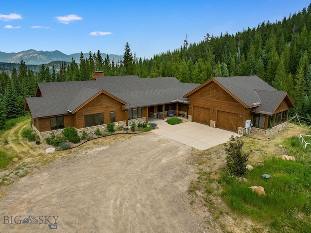 220 Watershed Rd, Big Sky, MT 59716 - view of front of home featuring stone siding, driveway, a view of trees, a chimney, and an attached garage