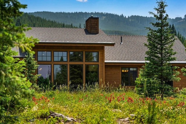 220 Watershed Rd, Big Sky, MT 59716 - back of house with a chimney, a wooded view, and roof with shingles