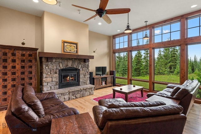 living room with a stone fireplace, ceiling fan, and light wood-type flooring