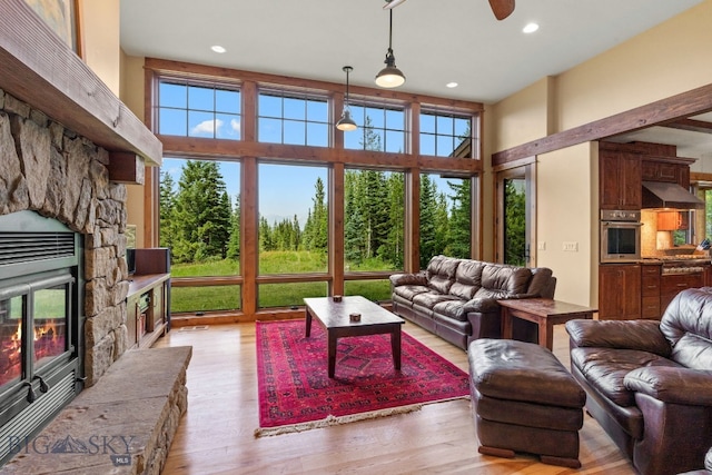 living room featuring a high ceiling, light hardwood / wood-style flooring, a stone fireplace, and a healthy amount of sunlight