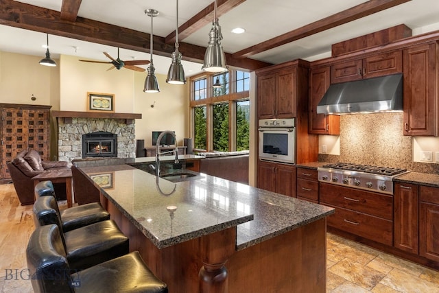 kitchen featuring appliances with stainless steel finishes, an island with sink, a kitchen breakfast bar, and beam ceiling