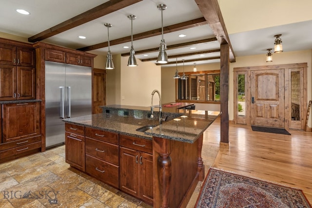 kitchen featuring a kitchen island with sink, sink, light hardwood / wood-style flooring, built in refrigerator, and beam ceiling