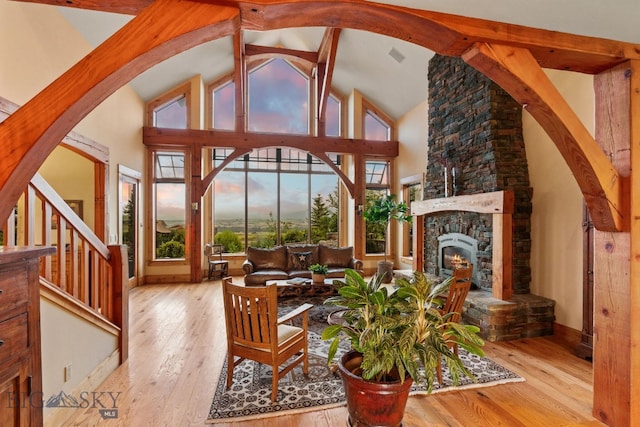 living room featuring light hardwood / wood-style floors, a stone fireplace, beamed ceiling, and high vaulted ceiling