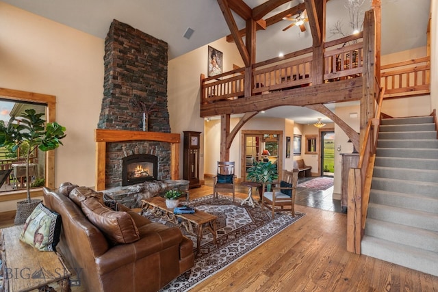 living room with high vaulted ceiling, a fireplace, beamed ceiling, wood-type flooring, and ceiling fan