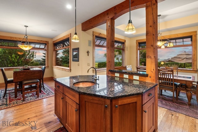 kitchen with dark stone counters, light wood-type flooring, hanging light fixtures, and sink