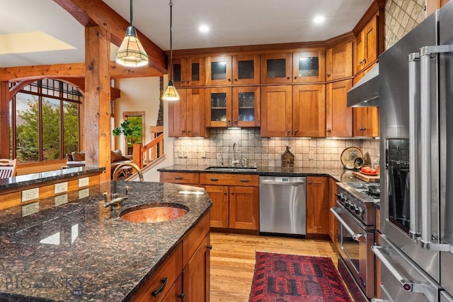 kitchen with light wood-type flooring, sink, decorative light fixtures, dark stone counters, and high quality appliances