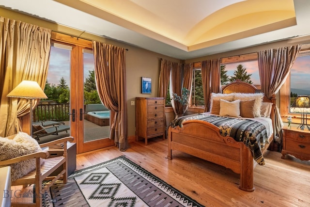 bedroom featuring wood-type flooring, a tray ceiling, access to exterior, and french doors