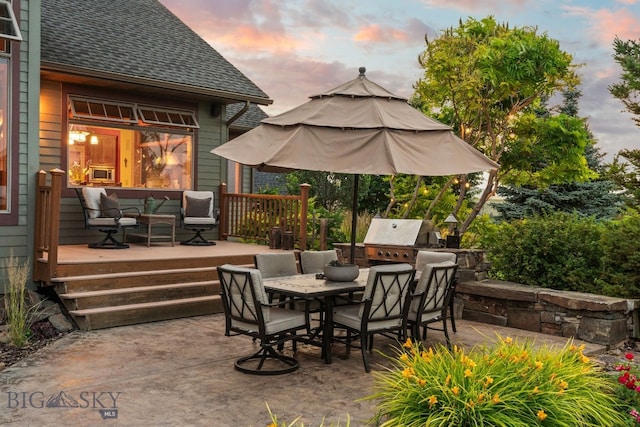 patio terrace at dusk with exterior kitchen, area for grilling, and a deck